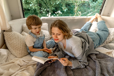 A girl reads a paper book to a little boy at a campvan, during summer time