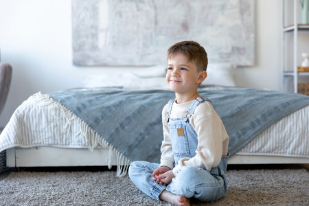 A a little boy sits at the white room, next to bed and smilesの写真素材