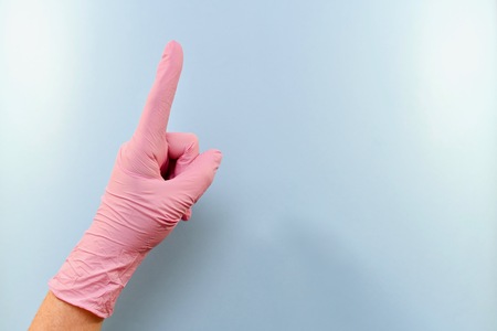 A hand in a pink medical rubber glove warns, threatens. On a blue background to the left.の写真素材