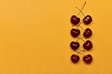 Red sweet cherry pairs in a row, pairwise crossed cuttings, on a yellow background, on the right. With drops of water.の写真素材