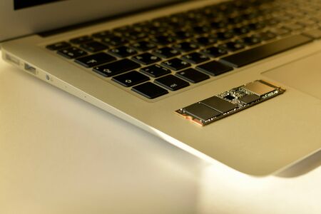Chip SSD-drive in the lower left corner of the laptop. Small parts of the chip are partially in sharpness. In the soft light of the beam. The keyboard is partially blurred.Neutral photo.の写真素材