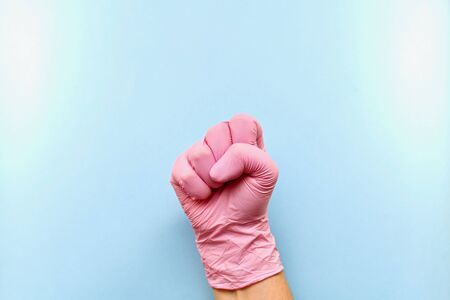 The right hand, clenched into a fist inside. In pink medical rubber gloves on a blue background, in the center, with a slope.の写真素材