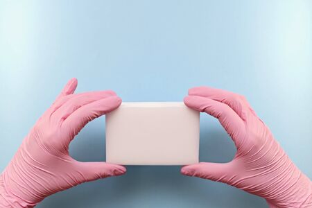 White household sponge from micro particles in white hands, dressed in pink rubber gloves. In the position of the horizontal screen. On a blue background.の写真素材