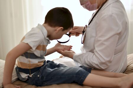 The kid leaned toward the magnifying glass and looked through it at his palm. Together with the doctor, sitting on the bed.の写真素材