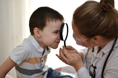The child makes a face and looks at the doctor through a magnifying glass that a woman in a white coat holds in her hands.の写真素材
