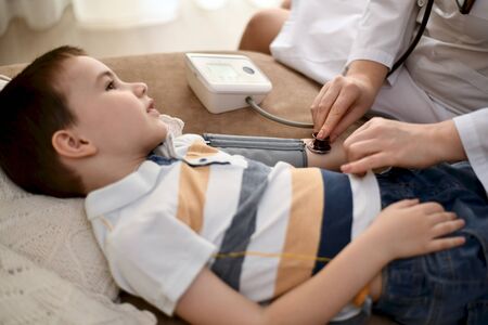 The boy lies on the bed and smiles, the doctor measures blood pressure with a tonometer.の写真素材