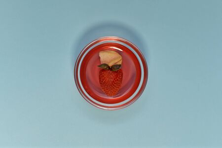 Dessert made from red marmalade with a slice of apples, strawberries and basil leaves. In a transparent round rosette tableware. Horizontally in the center on a blue background.の写真素材