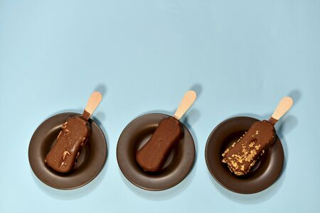 Three chocolate ice cream assorted, on a stick. Portioned, each in a separate saucer, on a blue background, below. View from above.の写真素材