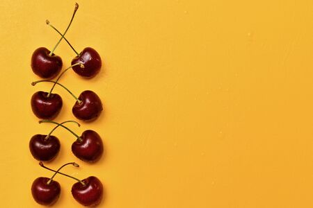 Red sweet cherry pairs in a vertical row, pairwise crossed cuttings, on a yellow background, on the left. With drops of water.の写真素材