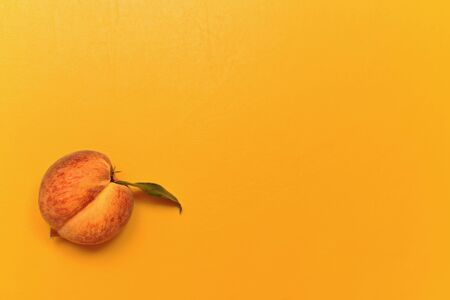 Ripe yellow-red peach with green leaf. With a longitudinal halfway dividing in half. On a yellow background in the lower left.の写真素材