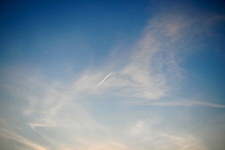 Airplane flying upward obliquely in a blue azure sky with blurred white clouds.の写真素材