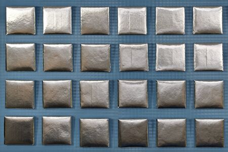 Aluminum chocolate squares in rows on a blue plastic background.の写真素材