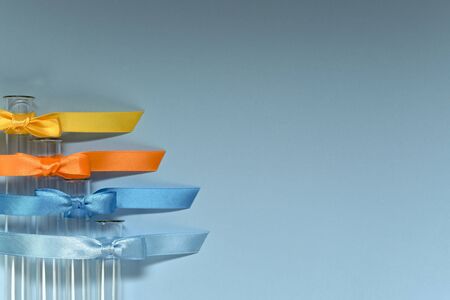 Empty glass test tubes located with a ladder and each tied with a satin ribbon of four colors and tied with a bow. On a blue background.の写真素材