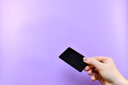 Giving a black credit or discount card with a hand on a purple background with free space.