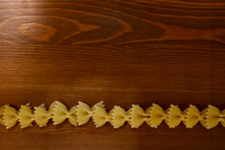 Line of pasta bows on a wooden background.