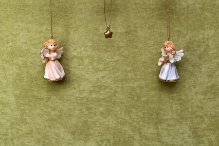 Christmas decorations, two angels in dresses look in the center at the star, suspended on gold threads on green plush matter, on top.の写真素材