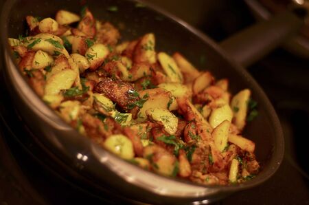 Potatoes fried with meat and herbs in a shiny frying pan against a dark background.の写真素材