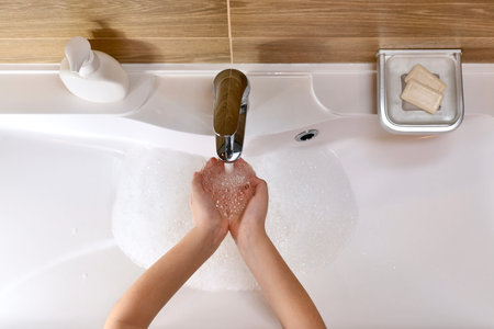 The baby's hands are folded under a jet of water in the sink in the bath, horizontal location, view...