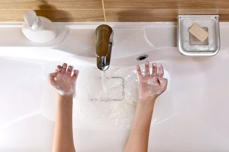 The child shows the palms rolled up the soapy foam-filled hands, with bent fingers, above the sink...