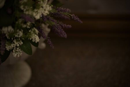 The background is made of a fragment of artificial white and purple flowers in a vase on the leg. A blurred dark frame image.の写真素材