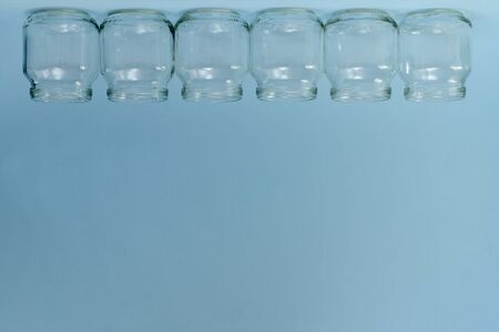 A horizontal row of six transparent inverted jars at the top of the frame on a blue free background.の写真素材