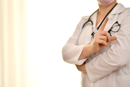 The doctor in a white robe with a stethoscope and glasses, shows a gesture of warning,...
