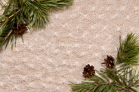 Christmas frame of pine branches with cones in two corners on a knitted light raft.