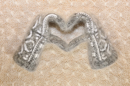 Woolly mittens are laid by the heart on a patterned down canvas.