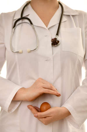 The doctor in a white robe, on one palm holds a chicken egg in the shell, the other hand on top protects.の写真素材