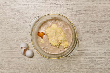 The stage of adding eggs to the yeast diluted in milk, in a glass transparent pan with handles. White egg halves of the shell, next to the left. The process of preparing the dough. On a countertop.の写真素材