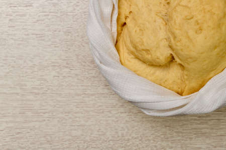 The puffed yeast dough has risen in a light large bowl, partially in the upper right corner on the countertop. Tied around with a braided white waffle towel. Fermentation of yeast in a flour mixture.の写真素材