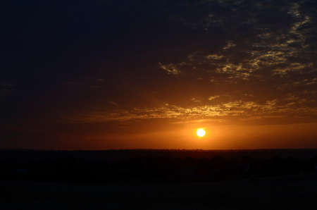 Orange sky with pearl clouds, and a flying silhouette of a bird. At sunset, with a white circle, the sun over the shadow of the earth.の写真素材