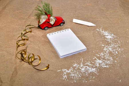 New Year composition from a red car with a bag of gifts, rides around a white notebook and a pencil with white shavings.の写真素材