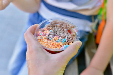 The hand of an adult gives the child a mini ice cream. Small multicolored balls.の写真素材