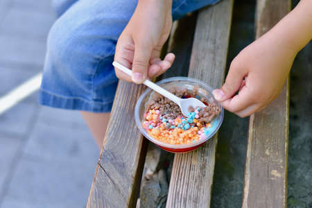 Children hands with a spoon, for eating mini small multicolored ice balls of fruit and chocolate ice cream.の写真素材