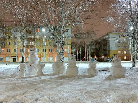 A company of a variety of snow-covered snowmen. On the street of the city in winter. Big and small,...