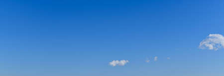 A panoramic photo of a clear blue sky with a soft smooth transition in tone, and light white floating clouds, diagonally in the lower right corner.の写真素材