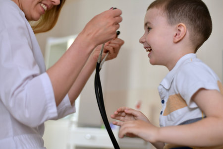The woman doctor invites the boy to try on his stethoscope. At the clinic for a consultation, fun...