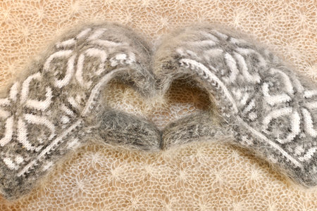 Gray white woolen mittens with a Christmas ornament in the form of a heart on a white openwork...