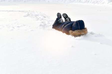 The child is playing in the snow. Lying buried his hands and head down, hid. On the feet, the shoes...