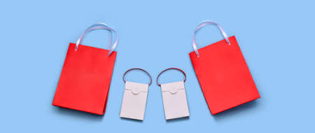 Paper shopping bags are two large reds and two white small ones, with handles made of satin ribbons. On a light blue wide background.の写真素材