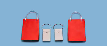 Paper shopping bags lined up in a horizontal row at the bottom. Two large reds around the edges and two small whites in the center. With satin ribbon handles. On a blue wide background.の写真素材