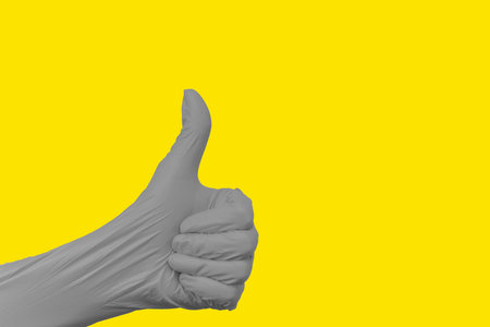 Gesture with a closed fist of the hand with the thumb extended upwards, wearing a protective...