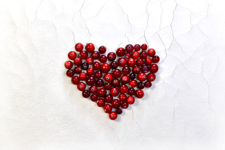 The heart is laid out, large in the center, with red glossy cranberries. On a white background with cracks and a rough matte texture.の写真素材