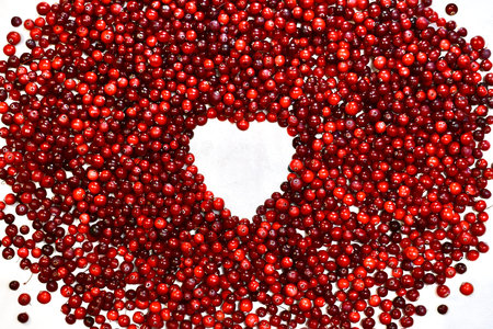A heart shaped frame made from cranberry berries. A white window surrounded by many red beads.