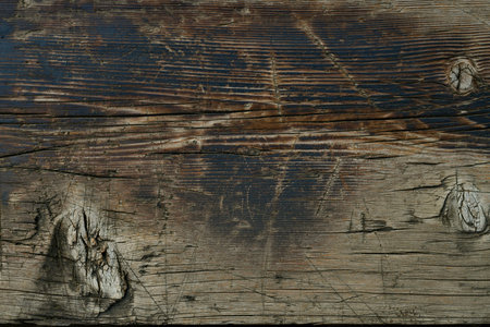 A wooden countertop with a visible edge of natural material with burnt areas, with a variety of textural knots, cracks and scratches on the background surface of gray brown black.の写真素材