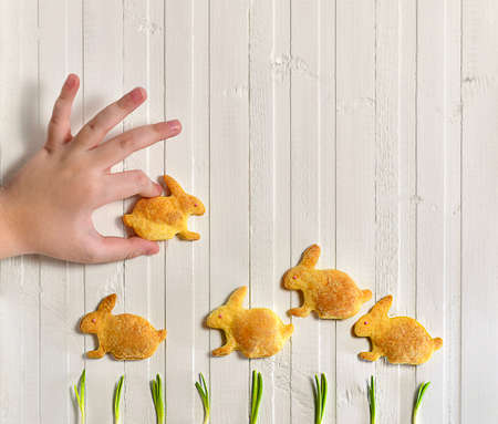 A child hand plays with cookies in the form of rabbits galloping on the green grass. View from above on white with vertical lines wooden background fence.の写真素材