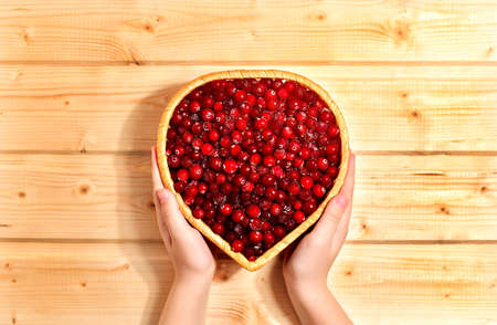 Ice cream red cranberry berries, in a wicker of vine basket in the shape of a heart. Carefully in hand on a wooden sunny warm background.の写真素材