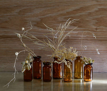 Glass dark bottles with dried herbs with seeds. On a wooden background, in yellow beige tones, the view from the front is consecrated by a ray of light.の写真素材