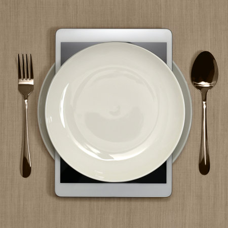 Elegant serving with glitter. Two white plates and a spoon with a fork made of yellow metal. Contactless ordering food online with a tablet, without a waiter.の写真素材